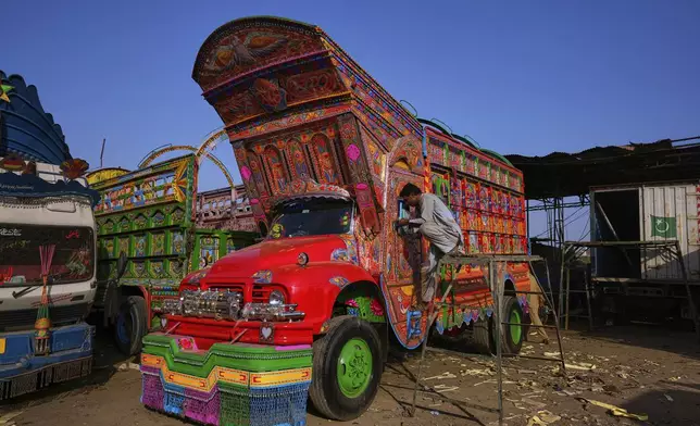 A worker fixes the side mirror of a newly refurbished decorated truck at a yard for workshops in Rawalpindi, Pakistan, Monday, April 21, 2025. (AP Photo/Anjum Naveed)