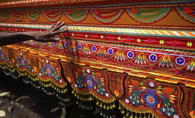 An artisan inspects the results after applying colorful stickers with traditional patterns on a newly refurbished truck at a yard for workshops in Rawalpindi, Pakistan, on Saturday, April 19, 2025. (AP Photo/Anjum Naveed)