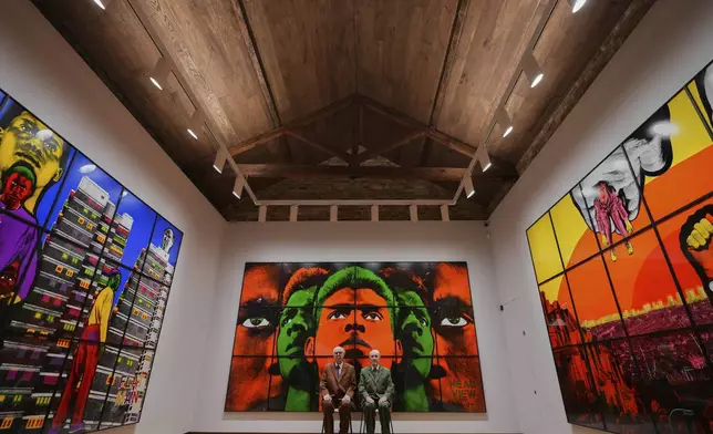 Art duo Gilbert &amp; George pose with artwork at their exhibition called 'DEATH HOPE LIFE FEAR…' an exhibition of 18 pictures by Gilbert &amp; George that span the years 1984 to 1998, at The Gilbert &amp; George Centre in London, Wednesday, May 14, 2025. (AP Photo/Kirsty Wigglesworth)