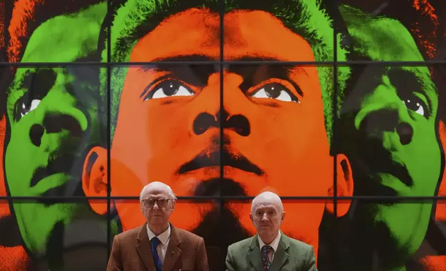 Art duo Gilbert &amp; George pose with artwork at their exhibition called 'DEATH HOPE LIFE FEAR…' an exhibition of 18 pictures by Gilbert &amp; George that span the years 1984 to 1998, at the Gilbert &amp; George Centre in London, Wednesday, May 14, 2025. (AP Photo/Kirsty Wigglesworth)