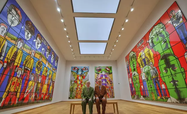 Art duo Gilbert &amp; George pose with artwork at their exhibition called 'DEATH HOPE LIFE FEAR…' an exhibition of 18 pictures by Gilbert &amp; George that span the years 1984 to 1998, at the Gilbert &amp; George Centre in London, Wednesday, May 14, 2025. (AP Photo/Kirsty Wigglesworth)