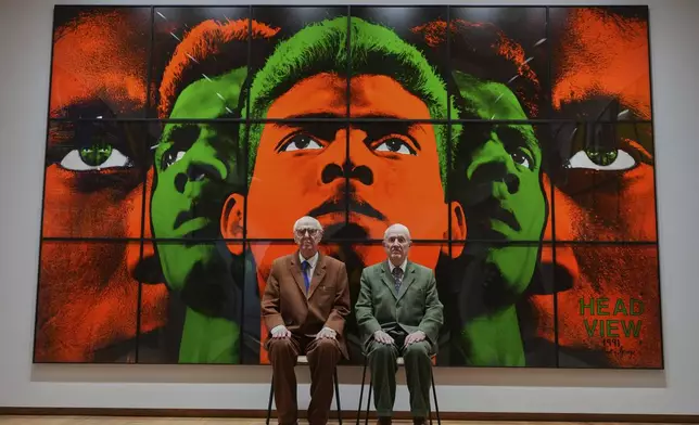 Art duo Gilbert &amp; George pose with artwork at their exhibition called 'DEATH HOPE LIFE FEAR…' an exhibition of 18 pictures by Gilbert &amp; George that span the years 1984 to 1998, at The Gilbert &amp; George Centre in London, Wednesday, May 14, 2025. (AP Photo/Kirsty Wigglesworth)