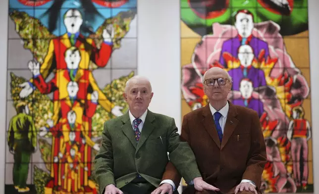 Art duo Gilbert &amp; George pose with artwork at their exhibition called 'DEATH HOPE LIFE FEAR…' an exhibition of 18 pictures by Gilbert &amp; George that span the years 1984 to 1998, at the Gilbert &amp; George Centre in London, Wednesday, May 14, 2025. (AP Photo/Kirsty Wigglesworth)