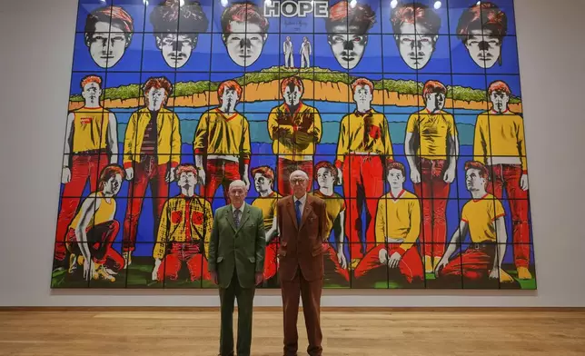 Art duo Gilbert &amp; George pose with artwork at their exhibition called 'DEATH HOPE LIFE FEAR…' an exhibition of 18 pictures by Gilbert &amp; George that span the years 1984 to 1998, at The Gilbert &amp; George Centre in London, Wednesday, May 14, 2025. (AP Photo/Kirsty Wigglesworth)