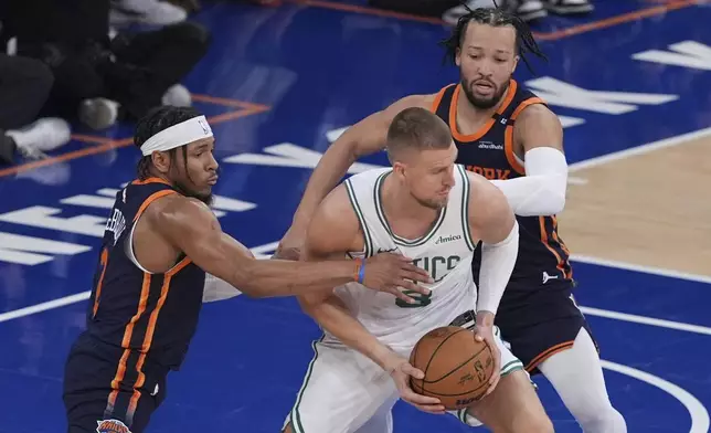 New York Knicks' Miles McBride, left, and Jalen Brunson, right, defend Boston Celtics' Kristaps Porzingis during the first half of Game 4 in the Eastern Conference semifinals of the NBA basketball playoffs Monday, May 12, 2025, in New York. (AP Photo/Frank Franklin II)
