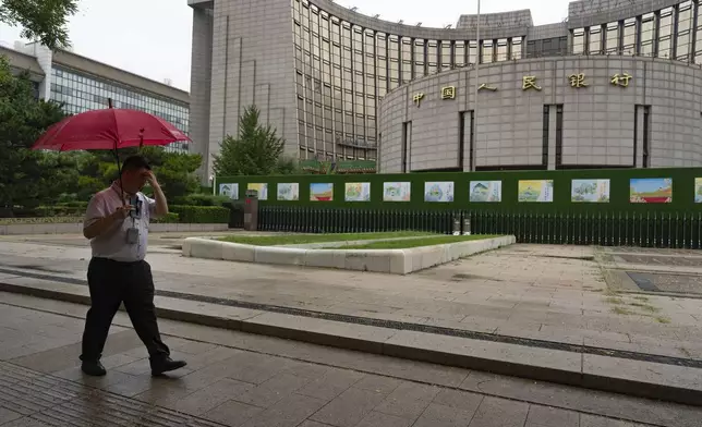 FILE - A man with an umbrella passes by China's central bank also known as People's Bank of China, in Beijing, Thursday, July 25, 2024. (AP Photo/Ng Han Guan, File)