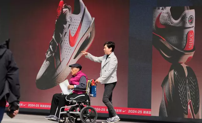 A woman pushes an elderly man past a Nike store at a mall in Beijing, Wednesday, May 7, 2025. (AP Photo/Ng Han Guan)