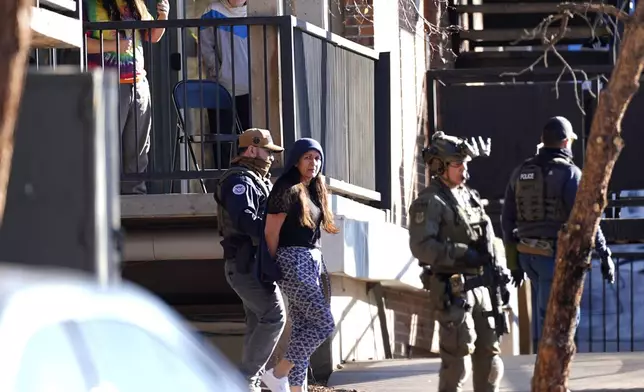 FILE - As a neighbor documents with a mobile telephone, a woman is escorted by a law officials from an apartment during a raid, Feb. 5, 2025, in east Denver. (AP Photo/David Zalubowski, File)