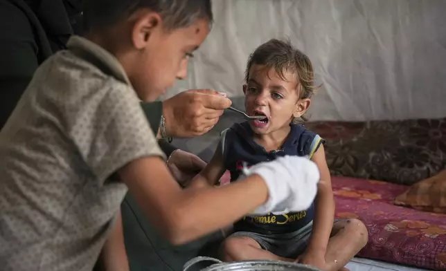 A little boy is fed by his mother with food from a community kitchen at the Muwasi camp for displaced Palestinians in Khan Younis, southern Gaza Strip, Sunday, May 18, 2025. (AP Photo/Abdel Kareem Hana)