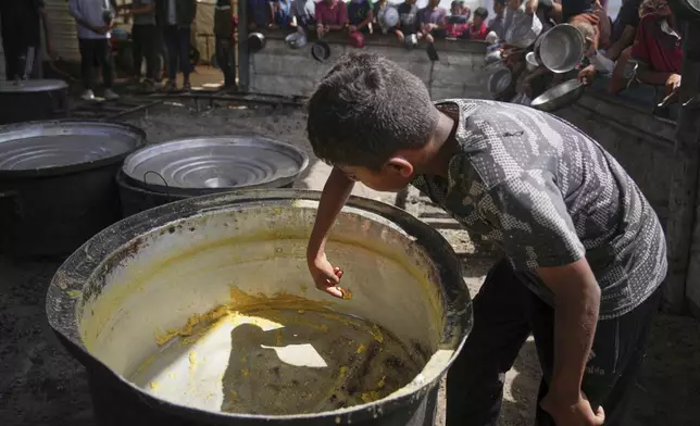A boy scrapes leftovers from an empty pot after all the meals were distributed at a community kitchen in Khan Younis, southern Gaza Strip, Wednesday, May 14, 2025. (AP Photo/Abdel Kareem Hana)