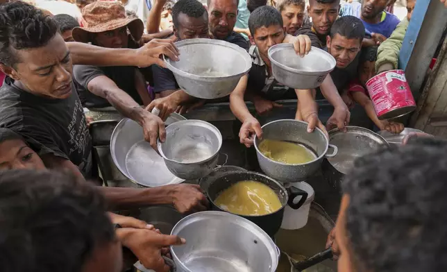 Palestinians struggle to receive cooked food distributed at a community kitchen in Khan Younis, southern Gaza Strip, Wednesday, May 14, 2025. (AP Photo/Abdel Kareem Hana)