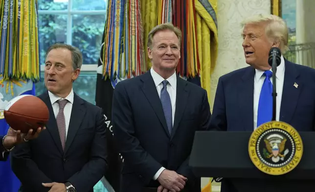 Washington Commanders owner Josh Harris, from left, and NFL Commissioner Roger Goodell watch as a football is presented to President Donald Trump during an event to announce that the 2027 NFL Draft will be held on the National Mall, in the Oval Office of the White House, Monday, May 5, 2025, in Washington. (AP Photo/Alex Brandon)