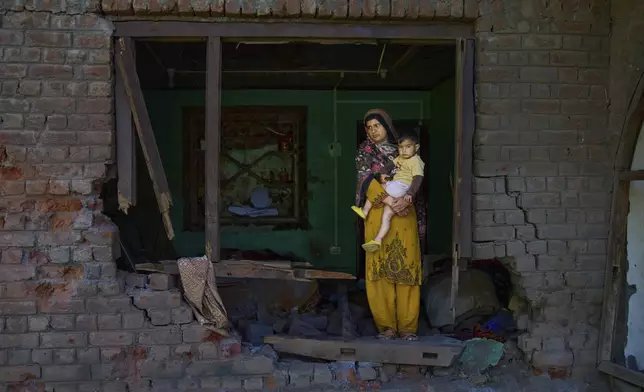 Nimarak holds her child as she inspects her house damaged by artillery shelling from Pakistan, in the border village of Gingal, north of Srinagar, Indian-controlled Kashmir, Wednesday, May 14, 2025. (AP Photo/Dar Yasin)