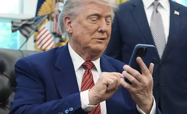 President Donald Trump silences his mobile phone which rang two times as he was speaking to reporters after signing executive orders regarding nuclear energy in the Oval Office of the White House, Friday, May 23, 2025, in Washington. (AP Photo/Evan Vucci)