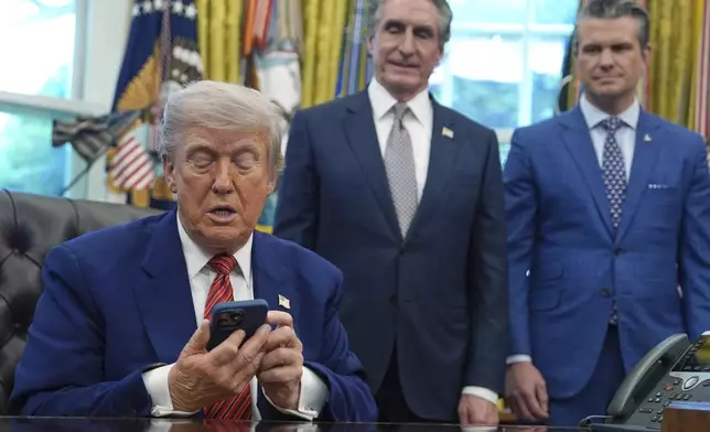President Donald Trump silences his phone that rang twice as he was speaking to reporters after signing executive orders regarding nuclear energy in the Oval Office of the White House, Friday, May 23, 2025, in Washington, as Interior Secretary Doug Burgum and Defense Secretary Pete Hegseth watch. (AP Photo/Evan Vucci)