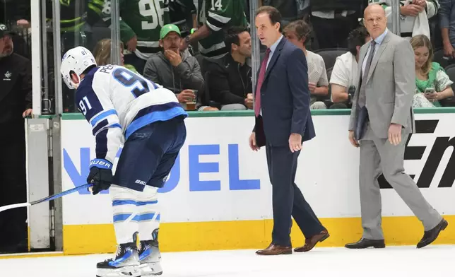 Winnipeg Jets head coach Scott Arniel, center, talks Cole Perfetti (91) as they and assistant coach Davis Payne, right, leave the ice after the team's loss to the Dallas Stars in Game 3 of a second-round NHL hockey playoff series in Dallas, Sunday, May 11, 2025. (AP Photo/Julio Cortez)