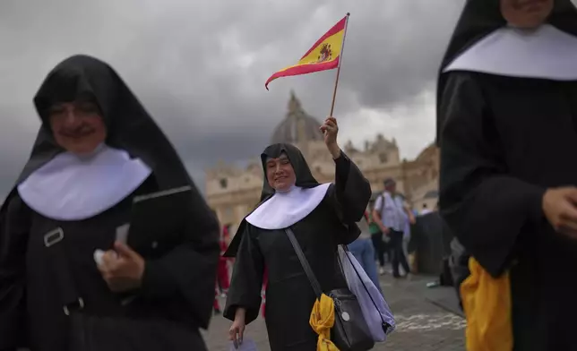 A nun waves a Spanish flag near St. Peter's Basilica, background, in Rome, on Wednesday, May 7, 2025, on the day cardinals sequester themselves at the Vatican for the start of a conclave to elect the 267th Roman pontiff, a successor to Pope Francis. (AP Photo/Francisco Seco)