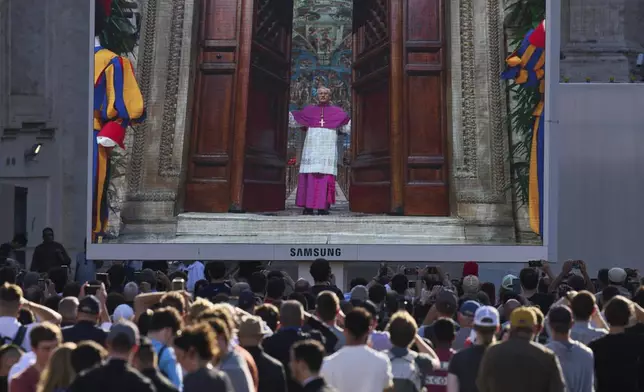 A giant screen in St Peter's Basilica shows Vatican Master of Ceremonies Archbishop Diego Giovanni Ravelli closing the doors to the Sistine Chapel after calling out "extra omnes", Latin for "all out," during the cardinals' conclave to elect a new pope at the Vatican, Wednesday, May 7, 2025. (AP Photo/Bernat Armangue)