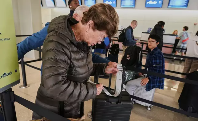 A woman checks her baggage tag as she waits in line at the Alaska Airlines counter, at Newark Liberty International Airport, in New Jersey, Friday, May 23, 2025. (AP Photo/Richard Drew)