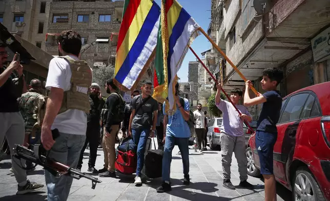 Druze boys hold their sect religious flags stand next to Druze gunmen, a day after clashes between members of the minority Druze sect and pro-government fighters left at least four people dead in the southern suburb of Jaramana, Damascus, Syria, Tuesday, April 29, 2025. (AP Photo/Omar Sanadiki)