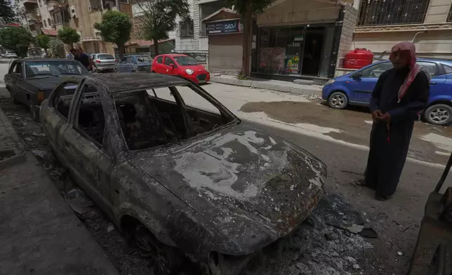 A man checks a charred car that was burnt after clashes erupted between members of the minority Druze sect and pro-government fighters, in the town of Sahnaya, south of Damascus, Syria, Thursday, May 1, 2025. (AP Photo/Omar Sanadiki)