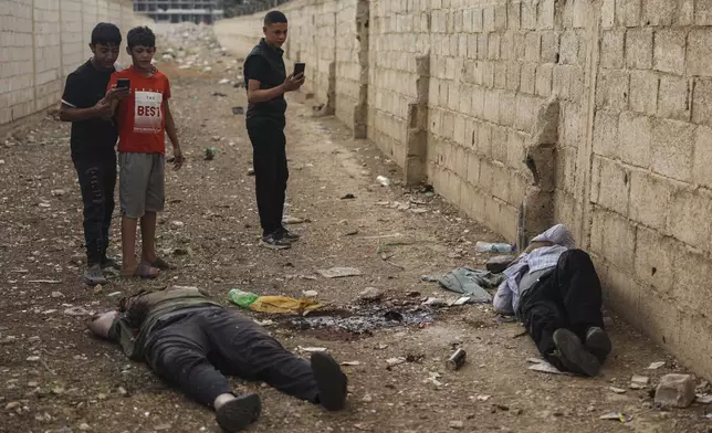 EDS NOTE: GRAPHIC CONTENT - Syrian boys take pictures with their mobile phones of the bodies of former Shanaya's town mayor Houssam Warawar and his son Haidar, who were killed in the town of Sahnaya, south of Damascus, Syria, Thursday, May 1, 2025, a day after clashes erupted between members of the minority Druze sect and pro-government fighters. (AP Photo/Ghaith Alsayed)