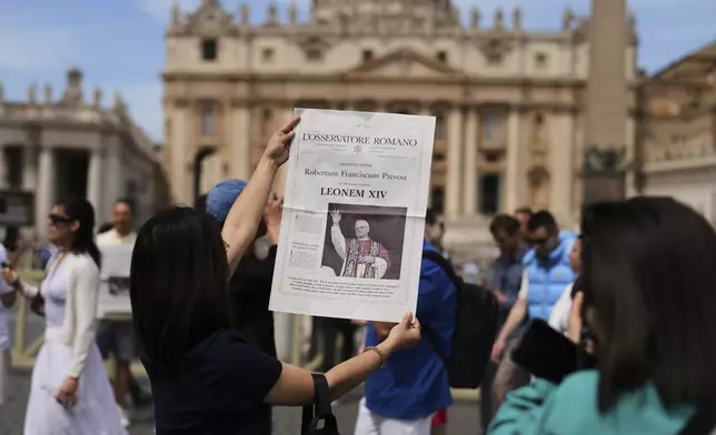 Tourists take photographs with a L'Osservatore Romano newspaper with the image of Pope Leo XIV at the Vatican, Friday, May 9, 2025, a day after he was elected history's first North American pope. (AP Photo/Francisco Seco)