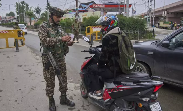 Indian paramilitary soldier checks the identity card of a scooterist at a temporary check point on the road leading to the airport after loud explosions were heard in Srinagar, in Indian controlled Kashmir, Saturday, May 10, 2025. (AP Photo/Dar Yasin)