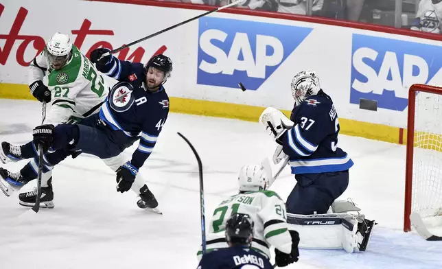 Winnipeg Jets goaltender Connor Hellebuyck (37) makes a save as Dallas Stars' Mason Marchment (27) dumps Jets' Josh Morrissey (44) during the first period of Game 2 of a second-round NHL hockey playoff series in Winnipeg, Manitoba, Friday, May 9, 2025. (Fred Greenslade/The Canadian Press via AP)