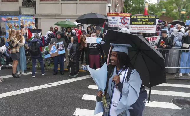 A graduate poses for a photo in front of a group of people protesting in support of Palestinians across the street from the main gates of Columbia University, Wednesday, May 21, 2025, in New York. (AP Photo/Heather Khalifa)