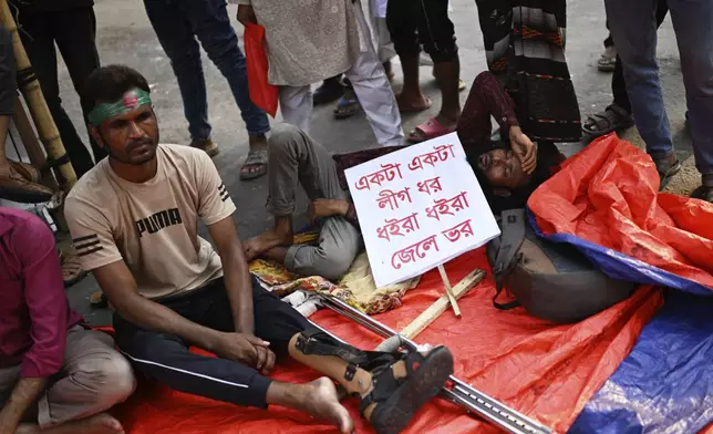 Protesters, who were injured in protests against former Prime Minister Sheikh Hasina last year, sit with a banner that reads 'One by one Awami League supporters should be detained and taken into custody' during a protest, in Dhaka, Bangladesh, Sunday, May 11, 2025. (AP Photo/Mahmud Hossain Opu)