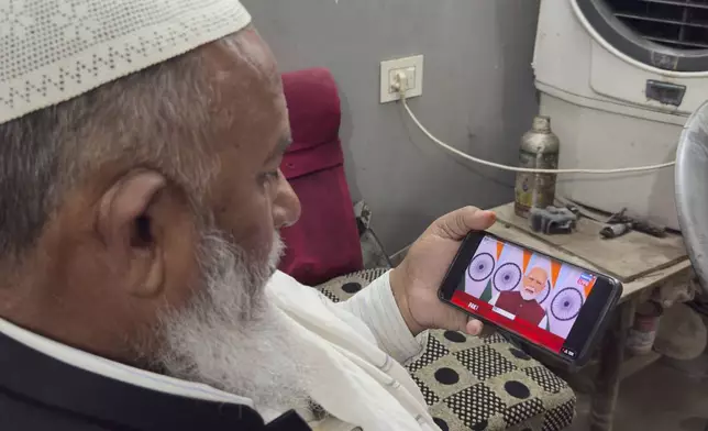 An Indian muslim shopkeeper watches on a phone the live telecast of Indian Prime Minister Narendra Modi's speech on television screens, in Prayagraj, in the northern Indian state of Uttar Pradesh, India, Monday, May 12, 2025. (AP Photo/Rajesh Kumar Singh)