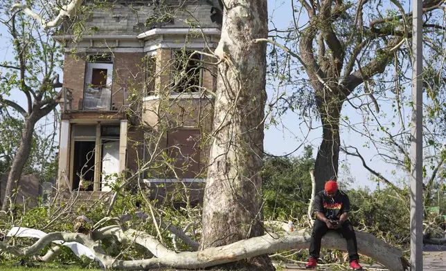 Steven Lampink sits on a downed tree after a severe storm moved through Friday, May 16, 2025, in St. Louis. (AP Photo/Jeff Roberson)