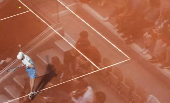 Germany's Yannick Hanfmann is reflected in a glass as he serves against Italy's Lorenzo Musetti during their first round match of the French Tennis Open at the Roland Garros stadium, in Paris, Sunday May 25, 2025. (AP Photo/Lindsey Wasson)