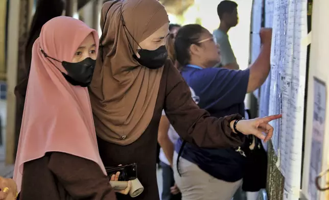 Residents look for their names in a registered voter list before casting their ballots at a polling station set up at a school in Davao City, southern Philippines, Monday, May 12, 2025. (AP Photo/Manman Dejeto)