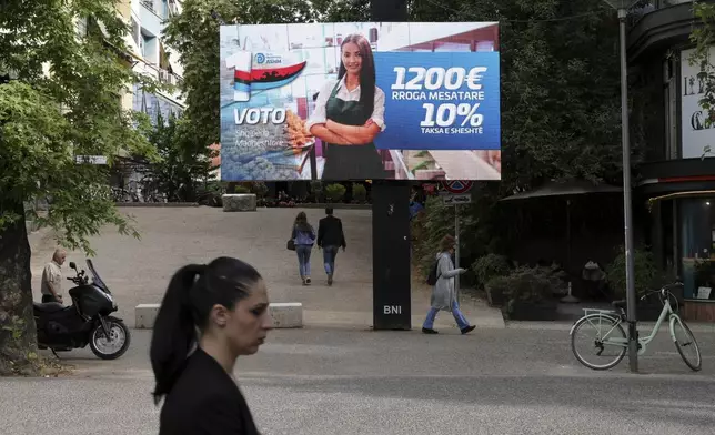 People pass a billboard of the opposition Democratic Party (ASHM) that reads "Vote Grandiose Albania, 1,200 euros average salary, 10% flat tax," in Tirana, Albania, Friday, May 9, 2025. (AP Photo/Vlasov Sulaj)