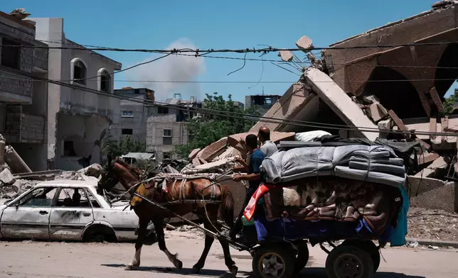 Smoke rises to the sky following an Israeli airstrike as Palestinians fleeing Jabalia move with their belongings in Gaza City, Friday, May 30, 2025. (AP Photo/Jehad Alshrafi)