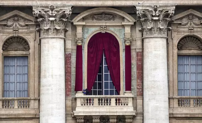 A man gives the last touch to a red drape wrapped around a column of the central lodge of St. Peter's Basilica in Vatican City, Monday, May 5, 2025, before the conclave starting on May 7, where they will elect the 267th pontiff of the Catholic Church. (AP Photo/Gregorio Borgia)