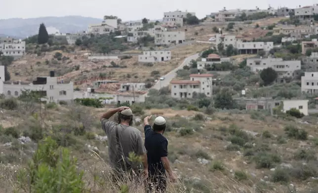 Israeli settlers look towards their neighboring village the morning after a Palestinian gunman killed Tzeela Gez, who was on her way to the hospital to give birth, outside of the West Bank settlement of Bruchin, Thursday, May 15, 2025. (AP Photo/Maya Alleruzzo)