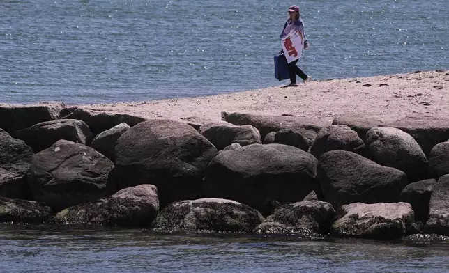 Audrey Constant, of Marshfield, Mass., is wrapped in a towel featuring the "Jaws" movie, while walking on a beach that was used as a filming location for the film five decades ago, Monday, May 12, 2025, in Edgartown, Mass., on Martha's Vineyard Island. (AP Photo/Charles Krupa)