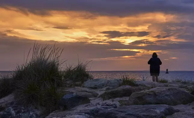 A woman views the sunset at Menemsha Beach, Wednesday, May 14, 2025, in Chilmark, Mass. (AP Photo/Robert F. Bukaty)