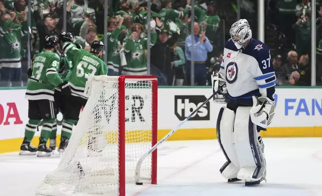 Winnipeg Jets goaltender Connor Hellebuyck reaches for the puck as the Dallas Stars celebrate a goal scored by Wyatt Johnston in the third period of Game 3 of a second-round NHL hockey playoff series in Dallas, Sunday, May 11, 2025. (AP Photo/Julio Cortez)