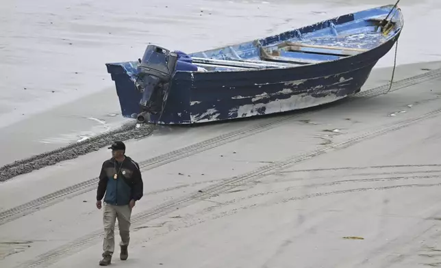 A law enforcement officer walks past capsized boat on the beach Monday, May 5, 2025, in at Torrey Pines State beach in San Diego, Calif. (AP Photo/Denis Poroy)