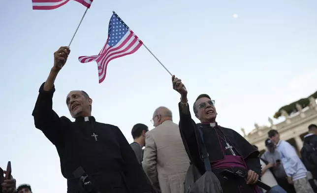 Clerics wave US flags during the speech of the newly elected Pope Leo XIV at the Vatican, Thursday, May 8, 2025. (AP Photo/Francisco Seco)