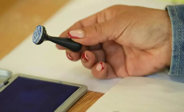 An election official holds a voting stamp while waiting for people to vote in the first round of the presidential election redo in Mogosoaia, Romania, Sunday, May 4, 2025. (AP Photo/Vadim Ghirda)