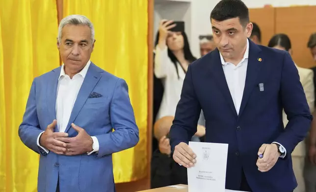 Calin Georgescu, winner of the first round of last year's annulled election, left, stands next to Presidential candidate George Simion as they cast their votes in the first round of the presidential election redo in Mogosoaia, Romania, Sunday, May 4, 2025. (AP Photo/Vadim Ghirda)