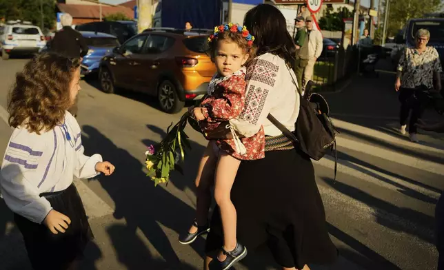 A woman carries a baby as she walks ahead of a media scrum around Calin Georgescu, winner of the first round of last year's annulled election, and Presidential candidate George Simion during in the first round of the presidential election redo in Mogosoaia, Romania, Sunday, May 4, 2025. (AP Photo/Vadim Ghirda)