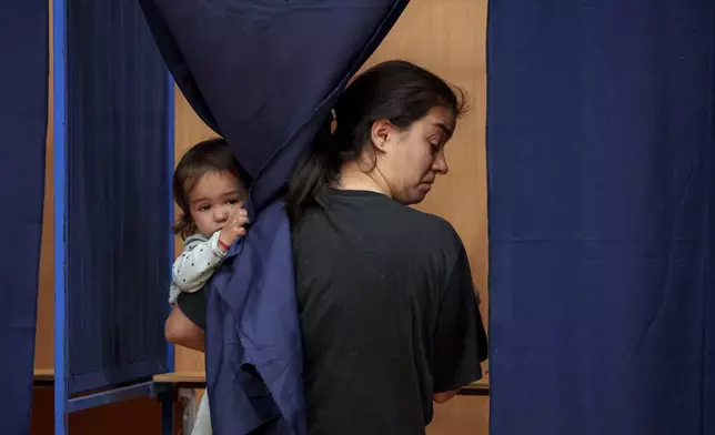 A woman holds a baby as she casts her vote inside a voting booth in the first round of the presidential election redo in Bucharest, Romania, Sunday, May 4, 2025. (AP Photo/Andreea Alexandru)