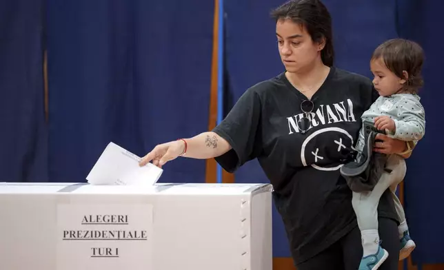 A woman holds a baby as she casts her vote in the first round of the presidential election redo in Bucharest, Romania, Sunday, May 4, 2025. (AP Photo/Andreea Alexandru)