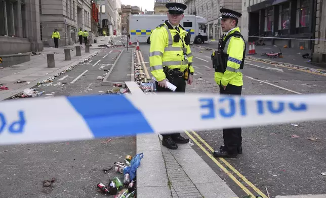 Police officers stand on the street where a 53-year-old British man plowed a minivan into a crowd of Liverpool soccer fans who were celebrating the city's Premier League championship Monday, injuring more than 45 people in Liverpool, England, Tuesday, May 27, 2025.(AP Photo/Jon Super)